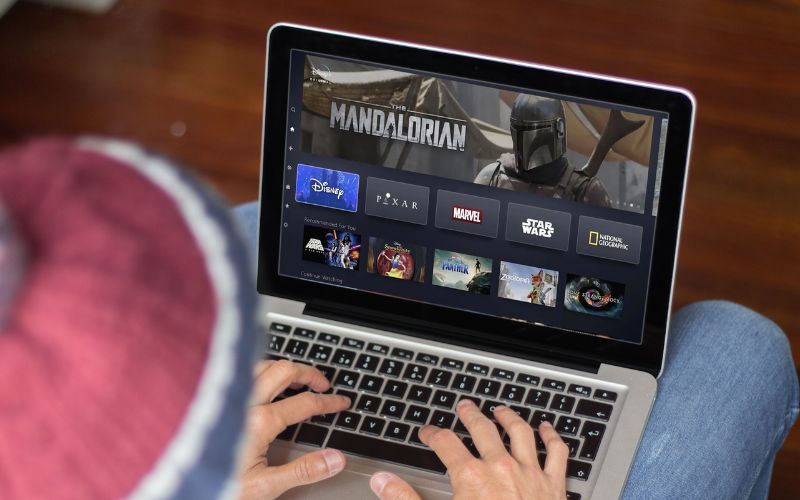 man is using his laptop to watch disney plus with The Mandalorian series on the main screen