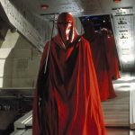 Three Imperial Royal Guards in crimson robes walking through an Imperial interior